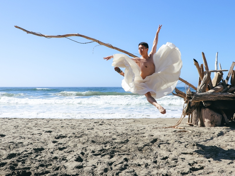 Meng jumping on the beach in a white dress.