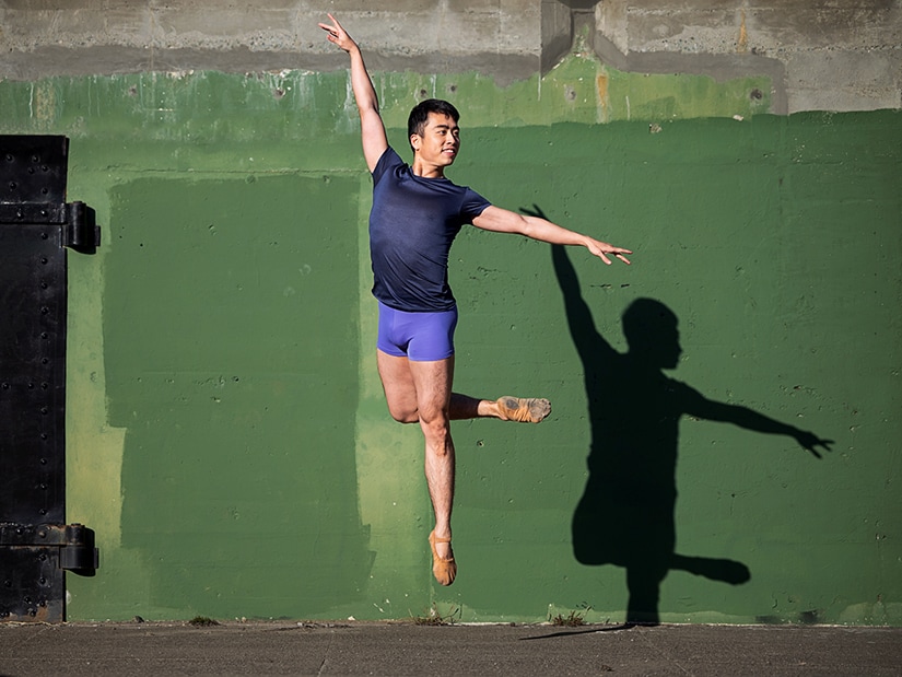 Meng jumping outside in front of a green wall.